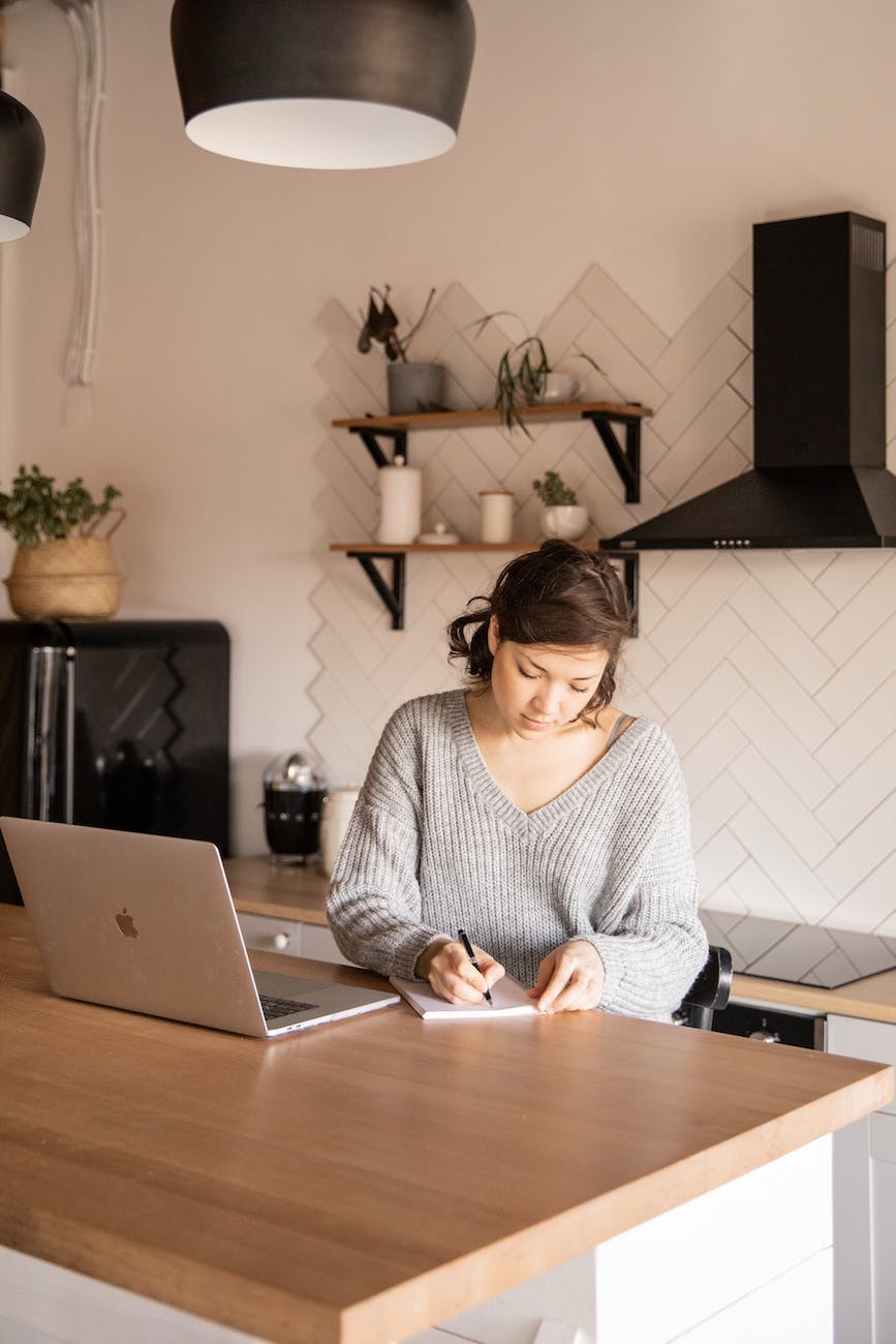 young female freelancer with laptop and notepad in kitchen